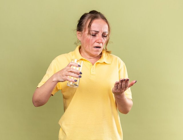 unhealthy-woman-yellow-shirt-feeling-terrible-holding-glass-water-pills-going-take-medicines-suffering-from-flu-cold-standing-green-wall_141793-100757.jpg