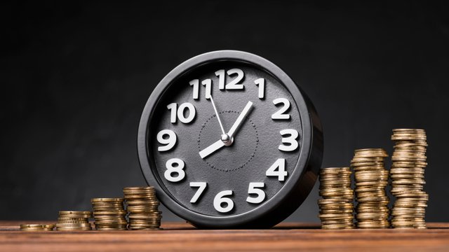 round-clock-increasing-coins-wooden-desk-against-black-backdrop.jpg