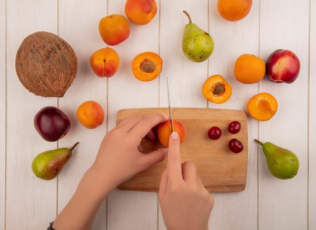 top-view-female-hands-cutting-apricot-with-knife-cherries-cutting-board-with-pattern-pears-peach-apricots-coconut-wooden-background_141793-25322.jpg