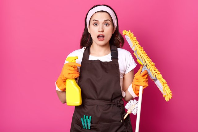 housewife-being-in-panic-because-she-has-so-much-things-to-clean-stands-with-open-mouth-keeps-detergent-spray-and-yellow-mop-in-hands-with-orange-gloves-shocked-girl-on-pink-studio-wall.jpg
