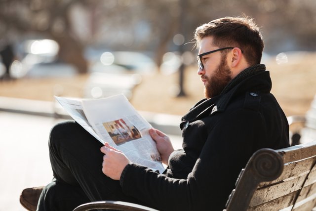 uomo-con-gli-occhiali-seduto-e-leggendo-il-giornale-in-citta.jpg