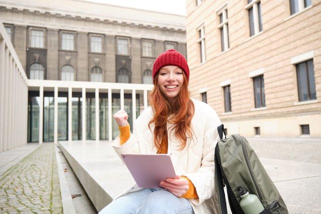 beautiful-redhead-woman-red-hat-sits-with-backpack-thermos-using-digital-tablet-outdoors-conn1.jpg