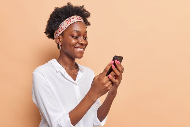 woman-holds-modern-mobile-phone-surfs-net-checks-newsfeed-social-networks-wears-headband-white-shirt-isolated-beige.jpg