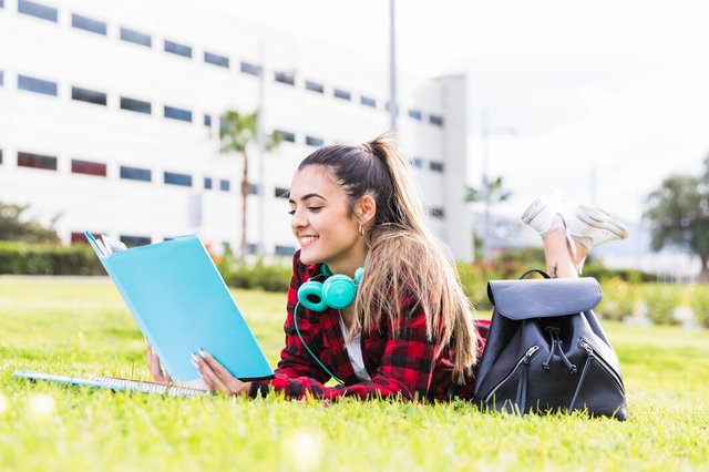 smiling-young-woman-laying-lawn-reading-book-university-campus_23-2148093571.jpg
