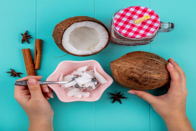 top-view-female-hands-holding-one-hand-spoon-with-pulps-coconut-other-hand-whole-coconut-with-cinnamonnise-glass-jar-blue.jpg