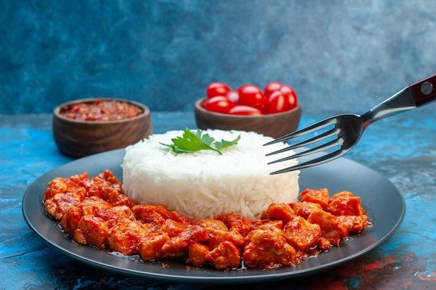 side-view-hand-holding-fork-rice-meal-with-chicken-sauce-black-plate-tomatoes-blue-background_140725-130448.jpg