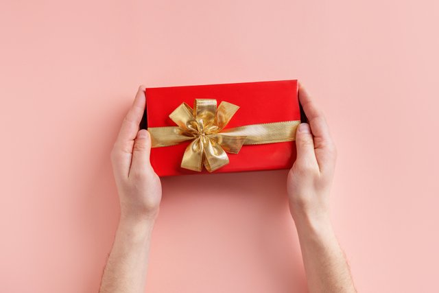 man-holding-giftbox-with-golden-ribbon-hands-pink-background.jpg