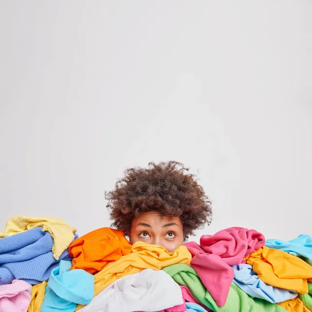 young-afro-american-woman-surrounded-by-different-colorful-clothes-sorts-out-wardrobe-focused-isolated-white-wall-blank-space-your-advertising-content-nothing-wear-concept_273609-52080.webp