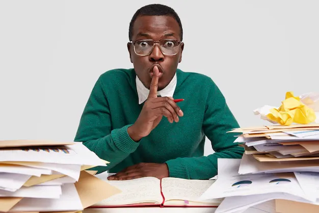 secret-african-american-male-ceo-shows-silence-sign-works-task-recieved-from-boss-writes-down-ideas-notebook-has-surprised-facial-expression_273609-23636.webp