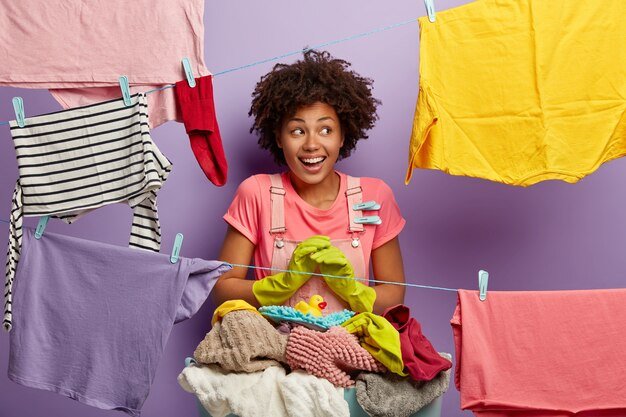 smiling-housewife-hangs-wet-clean-clothes-dry-rope-with-clothespin-wears-rubber-protective-gloves-busy-with-housework-weekend-isolated-purple-studio-wall-performs-home-duties_273609-26843.jpg