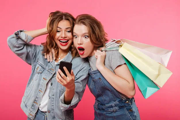 shocked-two-women-friends-holding-shopping-bags-using-mobile-phone_171337-5718.webp