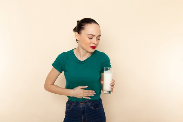 front-view-young-female-dark-green-shirt-blue-jeans-holding-milk-having-stomachache-beige.jpg