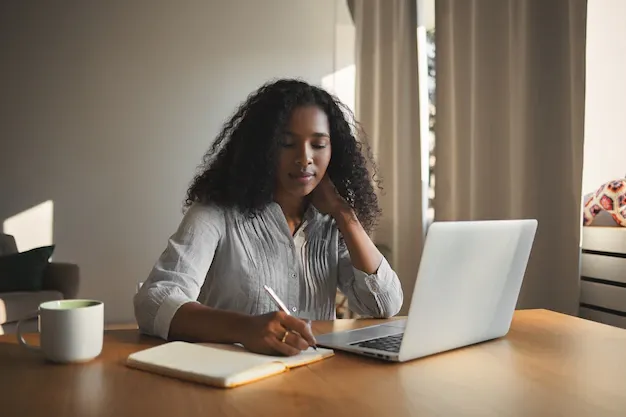 successful-attractive-young-afro-american-businesswoman-stylish-shirt-sitting-her-workplace-front-open-portable-computer-making-notes-her-diary-having-thoughtful-facial-expression_343059-1790.webp