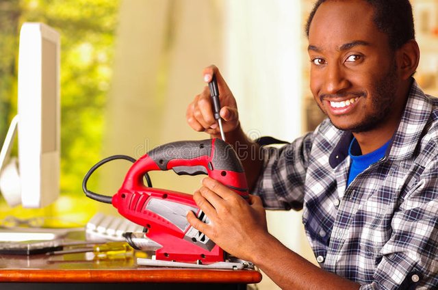 man-sitting-desk-repairing-handheld-jigsaw-using-screwdriver-smiling-happily-working-74262139.jpg