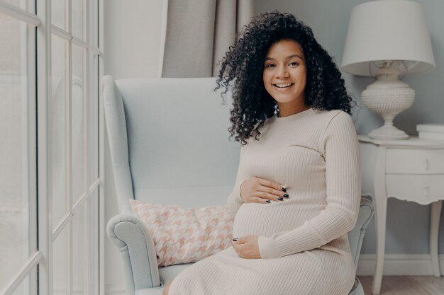 afro-american-adorable-smiling-pregnant-lady-beige-dress-sits-white-armchair_95891-4690.jpg