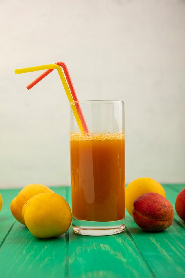 side-view-apricot-juice-with-drinking-tubes-glass-apricots-around-green-surface-white-background_141793-27290.jpg