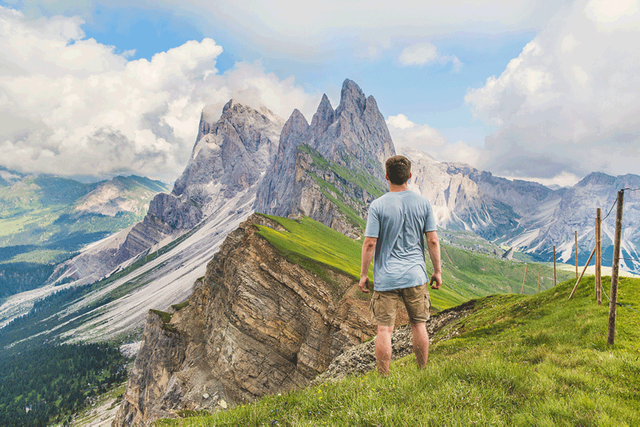 man standing on a mountain, staring off to a mountain