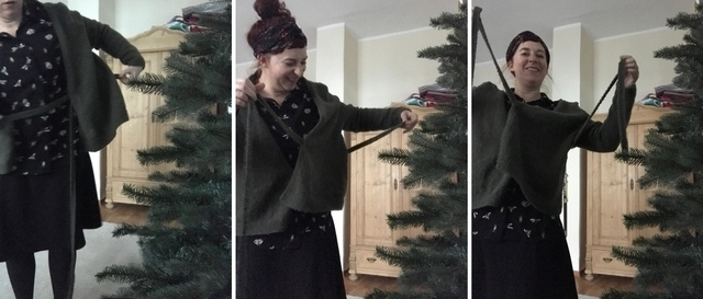 Laughing woman who stands besides a Christmas tree trying to fasten the wrap cardigan