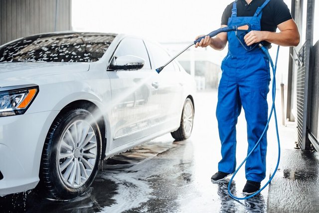 professional-washer-blue-uniform-washing-luxury-car-with-water-gun-open-air-car-wash_496169-333