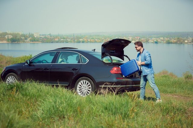 handsome-smiling-man-jeans-jacket-sunglasses-going-vacations-loading-his-suitcase-car-trunk-river-s-side_155003-32274