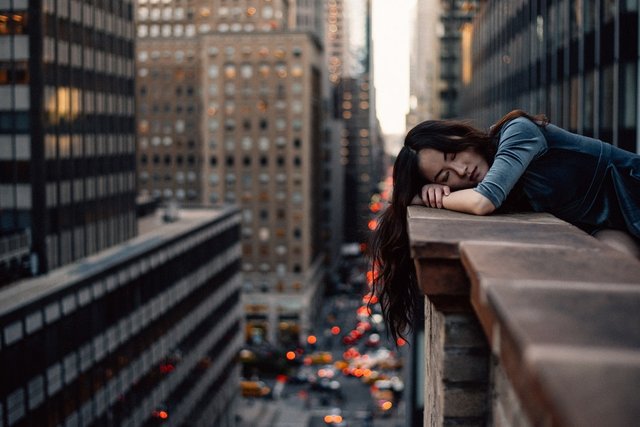 Woman with long-hair sleeping on the brick balcony edge among skyscrapers in New York