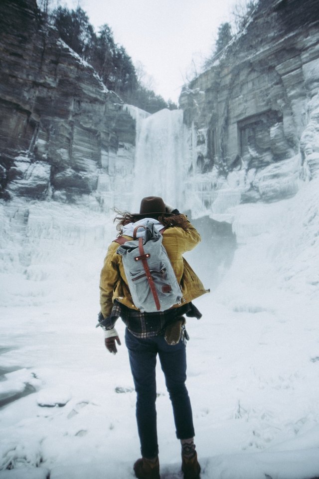 A hiker staring at a winter waterfall from the bottom of a mountain in Ithaca, New York