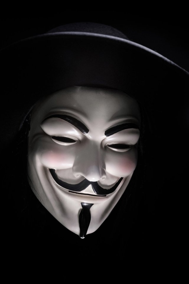 A smiling Guy Fawkes mask in shadow against a black background