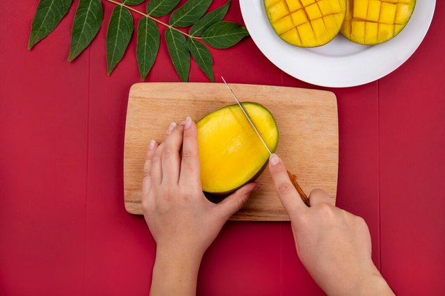 top-view-female-hands-cutting-mango-with-knife-woodenkitchen-board-with-sliced-mango-white-plate-with-green-leaf-red_141793-17220.jpg