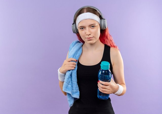 young-fitness-girl-sportswear-with-headphones-towel-her-neck-holding-bottle-water-standing-purple-wall_141793-50124.jpg