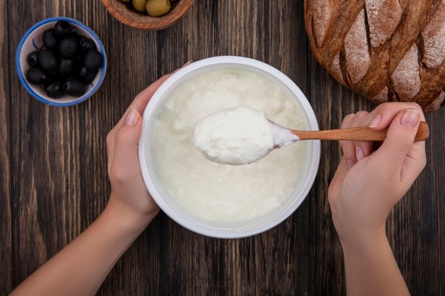 top-view-woman-eating-yogurt-bowl-with-wooden-spoon-olives-black-bread-wooden-background_141793-52123.jpg