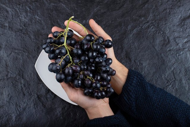 male-hands-holding-bunch-black-grapes-black-background_114579-42345.jpg