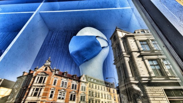 Spiegelung im Schaufenster: Die Stadt und die Maske.