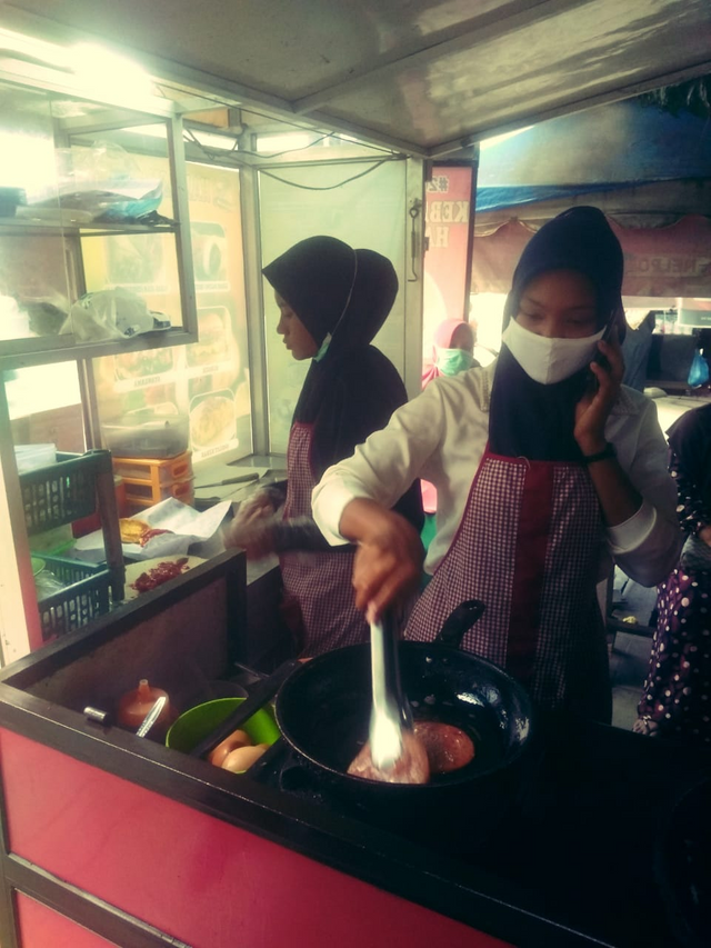 a seller looks serious when cooking even in the middle of a corona pandemic but still wearing a face mask