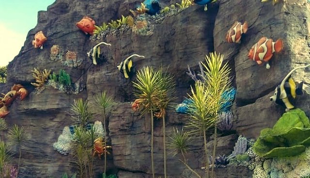 There are trees, flowers, and fish hanging on big rocks,