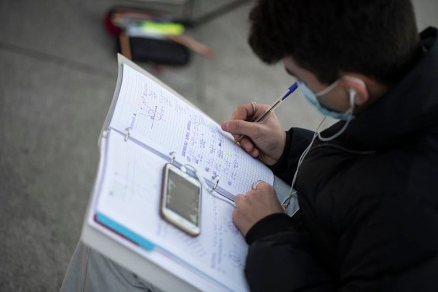 A student followed an online lesson on his mobile phone as he sat with others outside.