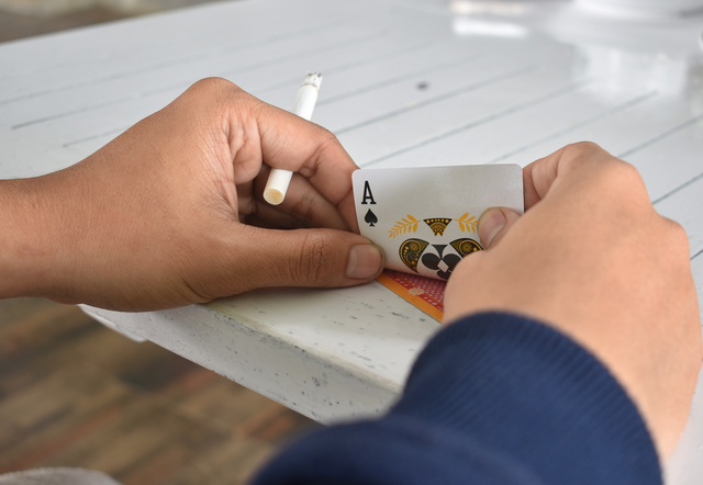 man's hand holding a cigarette and a card on the top of the table