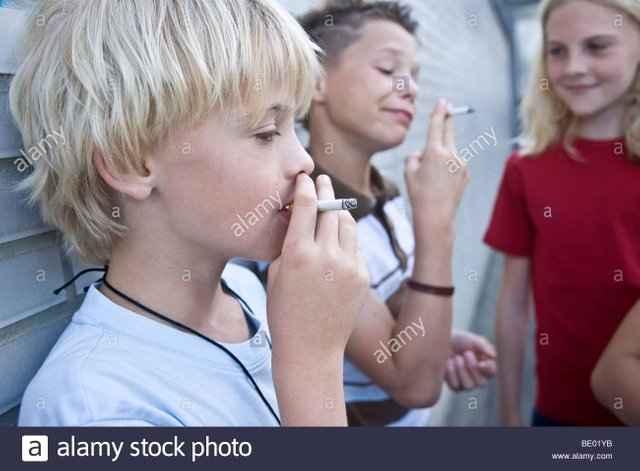 two-young-boys-smoking-a-cigarette-a-girl-watching-BE01YB.jpg