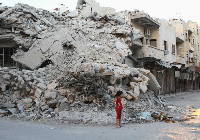 girl-stands-by-building-damaged-by-syrian-forces-data.jpg