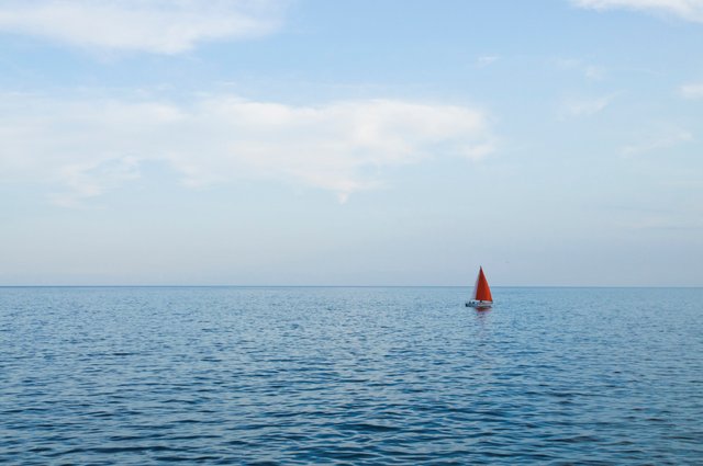 73.Sail boat with a red sail cruising in the calm waters of the evening..jpg