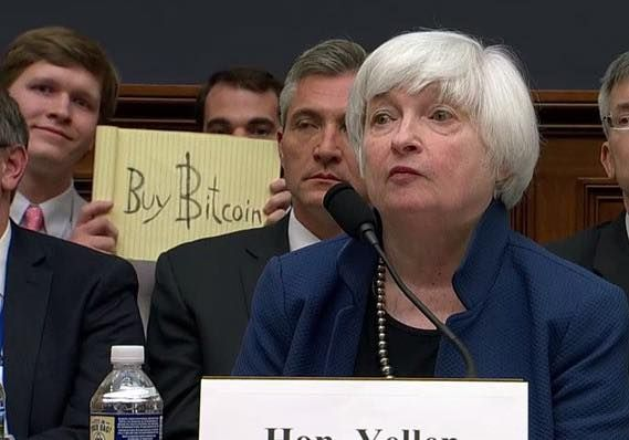Guy holding up "Buy Bitcoin" sign behind Janet Yellen during her testimony to congress on July 12th 2017