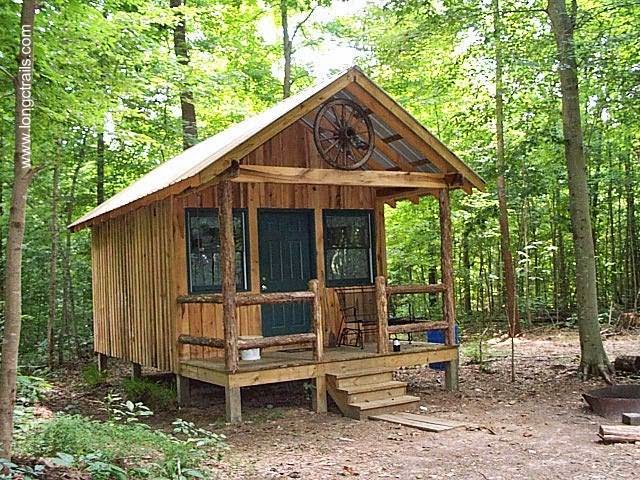 Cabaña pequeña de madera rústica con porche de entrada y una rueda de carro como ornamento.JPG