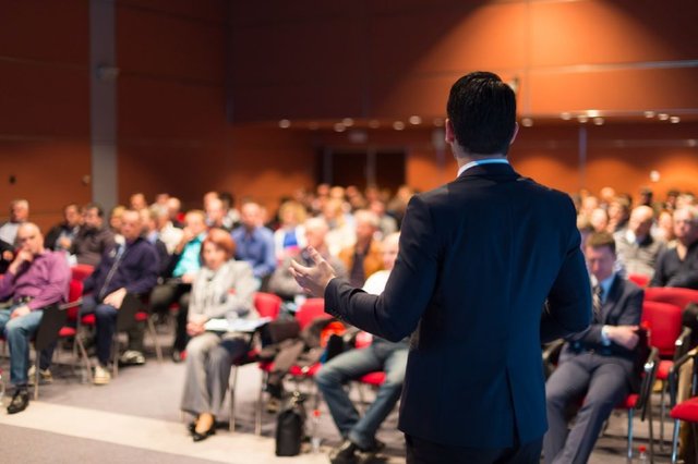 Hombre-con-traje-dando-una-charla-delante-de-varias-personas-en-una-sala-de-conferencias.jpg