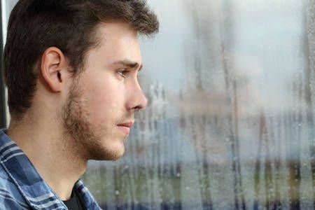 53115446-vista-lateral-de-un-anhelo-hombre-y-mirando-por-la-ventana-en-un-d-a-de-lluvia-triste.jpg