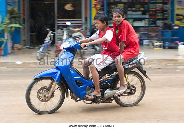 two-boys-brave-the-elements-on-a-motorbike-in-sisophon-cambodia-cy68nd.jpg