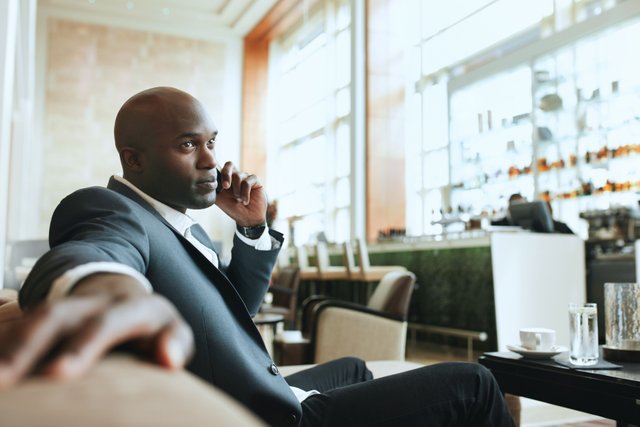 african-business-man-talking-on-mobile-phone-while-waiting-in-a-hotel-lobby-young-business-executive-using-cell-phone-while-waiting-at-lounge_r6BGDrVKe_tn.jpg