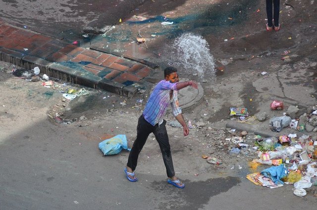 Man having fun for Holi in a garbage lined street in Delhi.jpg