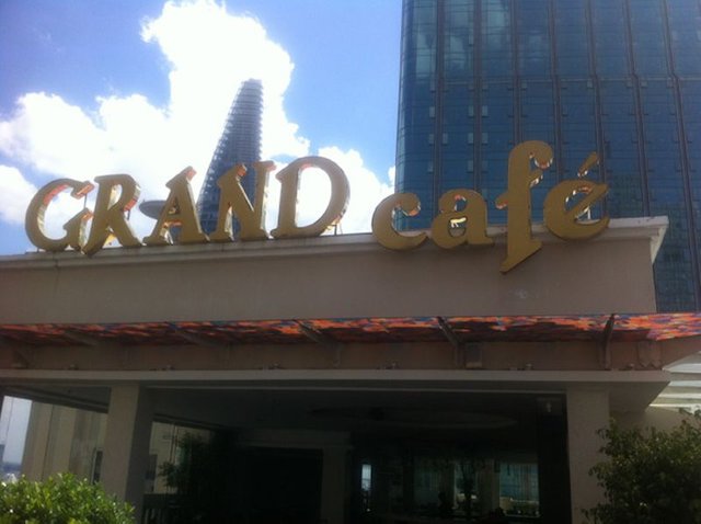 The Bitexco Tower and Saigon Times Square towering over the Grand Cafe sign.jpg