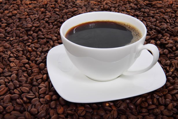 Cup of coffee in saucer, sitting surrounded by coffee beans.
