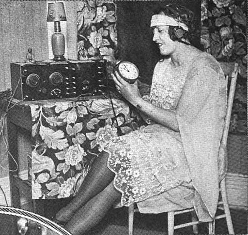A young woman setting her clock back after the end of daylight savings time using time signals sent by radio. Author unknown. Public Domain.