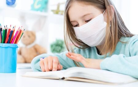 Cute Schoolgirl In Medical Face Mask Studying At Home Stock Photo ...